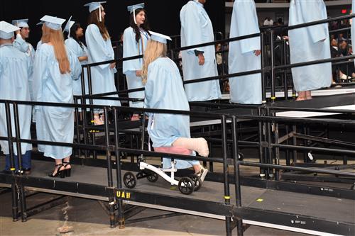 student with broken leg on scooter to stage to get diploma